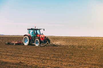 Fototapeta premium Farmer in tractor preparing land with seedbed cultivator as part of pre seeding activities in early spring season of agricultural works at farmlands.