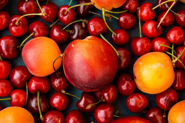 Ripe glossy sweet cherries with water drops, nectarines, apricots scattered on dark blue background, seamless pattern, template, vibrant colors
