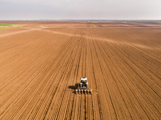 Aerial shot of a farmer seeding, sowing crops at field. Sowing is the process of planting seeds in...