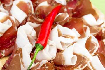 Slices of Prosciutto and red hot pepper on wooden plate .