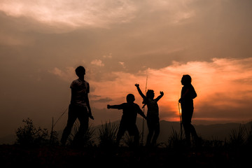 Fototapeta na wymiar Group of happy children playing on meadow at sunset, silhouette