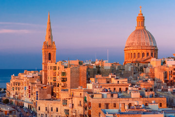 View from above of the domes of churches and roofs at beautiful sunset with churches of Our Lady of Mount Carmel and St. Paul's Anglican Pro-Cathedral, Valletta, Capital city of Malta - obrazy, fototapety, plakaty
