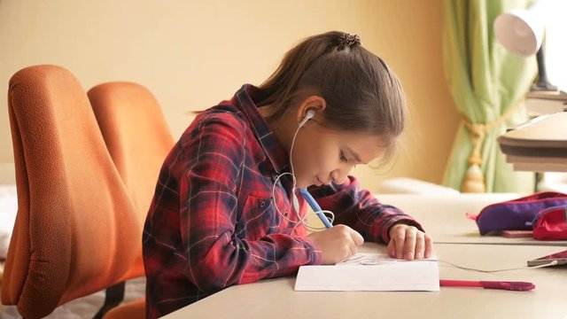 4k video of teenage girl listening music with earphones while doing homework at bedroom