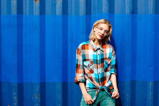 Portrait of a young girl of the blonde in glasses on a background the blue iron wall
