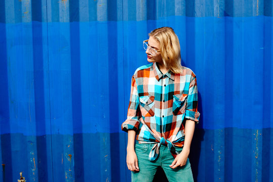 Portrait of a young girl of the blonde in glasses on a background the blue iron wall