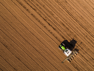 Obraz premium Aerial shot of a farmer seeding, sowing crops at field. Sowing is the process of planting seeds in the ground as part of the early spring time agricultural activities.
