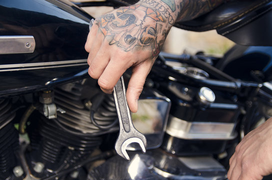 Closeup, tattooed man hand holding wrench making modifications to motorcycle 