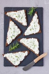 Pumpernickel bread with feta, cream cheese, rosemary, lemon and garlic dip, on slate board, top view, vertical