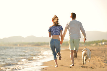 two young people running on the beach kissing and holding tight with dog