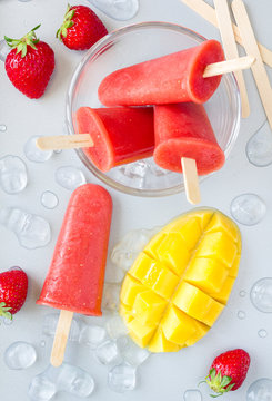 Homemade strawberry-mango popsicles on a gray background