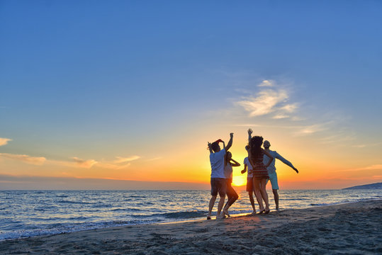 group of happy young people dancing at the beach on beautiful summer sunset