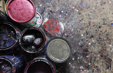 old paint cans with color splashes on cement floor. over light