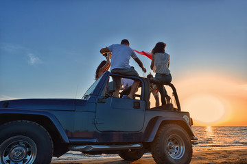 Five young people having fun in convertible car at the beach at sunset. - obrazy, fototapety, plakaty