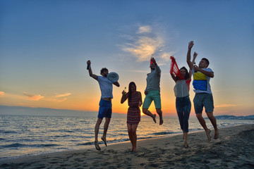 Group of happy young people is running on background of sunset beach and sea
