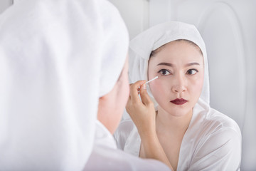 woman looking mirror and remove makeup beside eye with a cotton swab