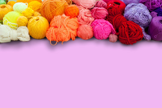 Colorful yarn stacked in a series of colors. Background pink. Balls and skeins of colored yarn for knitting.