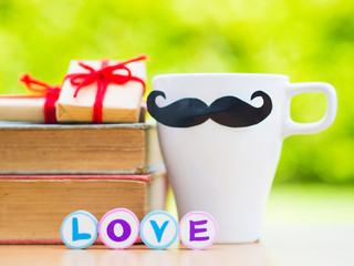 Father's day concept. LOVE DAD alphabet on stack of books, gifts, tea cup with black Mustache and flower on background