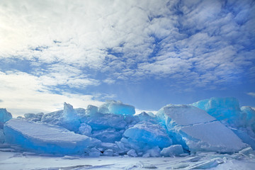 Fototapeta premium Hummocks of turquoise blue ice blocks covered with snow under white clouds