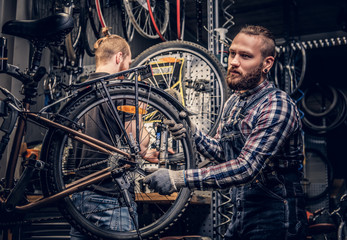Two bearded mechanics fixing bicycle's wheel in a workshop.