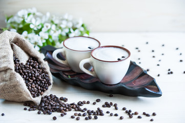 Two cups of freshly brewed, frothy cappuccino. Spilled coffee grains, chocolate and cane sugar. Theme of coffee, cappuccino, mocha chino, america no. Beautiful elegant background with place for text
