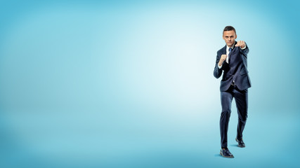 A serious businessman in front view throwing punches while standing on blue background.