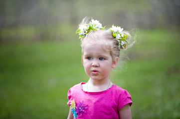 A little girl in a pink T-shirt in the summer for a walk in the clearing. The girl yawns, walks, collects flowers, looks at the lizard.