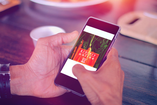 Hand Holding Mobile Phone With Grocery Online Text On Screen On Wooden Table Background In Kitchen