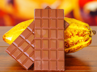 Close up of a fresh cocoa pods and chocolate bar over a wooden table