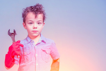 Cute little boy in a blue shirt and red rubber gloves holding a wrench