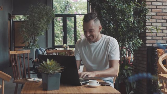 Handsome crazy emotional young happy male guy businessman shows success in cosy cafe. Man work on compter, smiling in front of laptop.