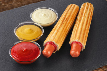 French hot dog and bowls with sauces on a slate board. Fast food.