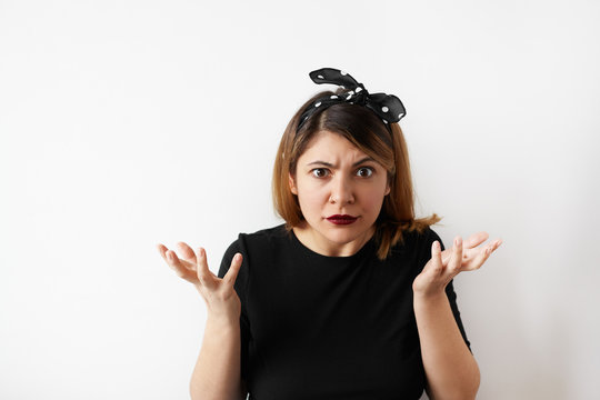 Human negative emotions and feelings. Indoor studio shot of puzzled Caucasian young woman wearing black dress with arms out raising one brow, having indignant and surprised facial expressions.