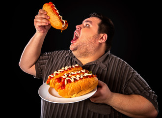 Diet failure of fat man eating fast food hot dog on plate. Breakfast for overweight person who...