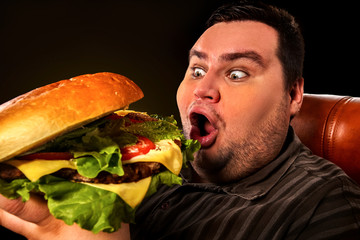 Diet failure of fat man eat fast food . Breakfast for mad overweight person who eating huge hamburger. Junk meal leads to obesity concept on black background.