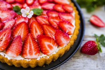 Delicious sponge cake with fresh strawberries and mascarpone on a wooden background.