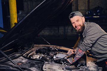 Bearded tattooed mechanics near car in a garage.