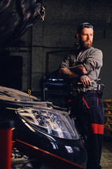 Obraz na płótnie Canvas Bearded mechanics with crossed arms posing near a car.
