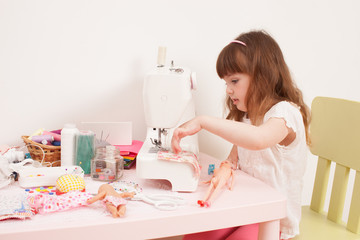 Obraz na płótnie Canvas Girl sews dress dolls from pieces of fabric