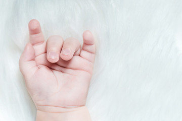 Hand of a baby with a goat gesture on a white fluffy background