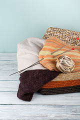 Ball of wool, needles and woolen sweater with spokes for handmade knitting in basket on wooden table.