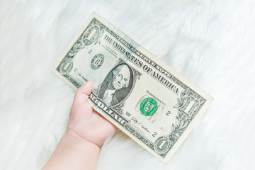 Baby hand holds a dollar on a white fluffy background