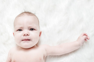 Crying baby lies on a white fluffy background