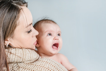 Woman in a sweater holds a crying baby in her arms