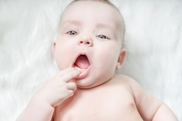 Cute baby lying on a white fur  with fingers in the mouth