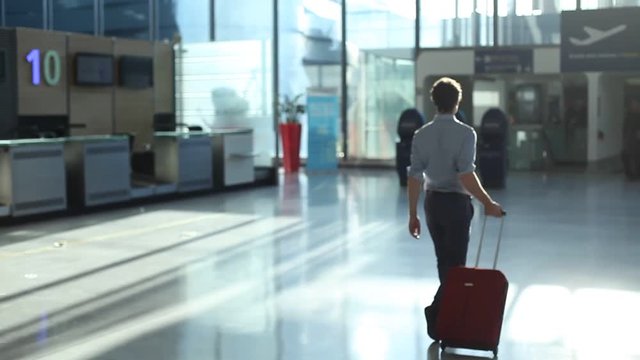 businessman with suitcase walking in modern airport interior, business travel