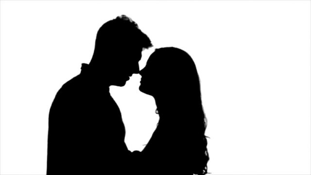 Loving couple look at each other and begin to kiss. Silhouette. White background. Slow motion