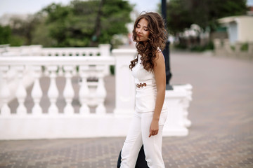 Beautiful stylish brunette girl, street portrait, street fashionable look. Beautiful woman with long hair in white clothes and a handbag in her hands, a strict style, walking on the street