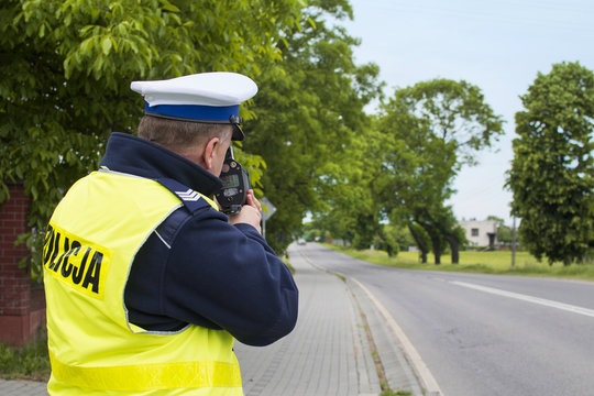 Kontrola radarowa przy drodze wojew&oacute;dzkiej. Policjant dokonuje pomiaru prędkości w terenie zabudowanym.