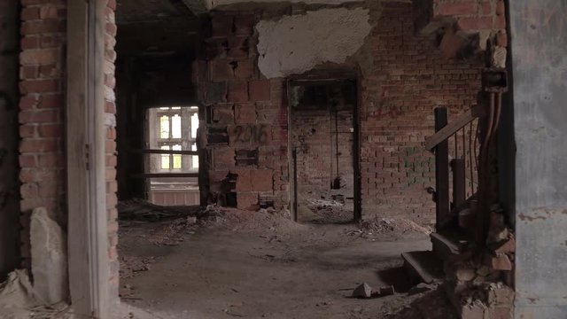 FPV, CLOSE UP: Urbexing old decaying abandoned hotel, walking across the dark scary crumbling rooms with broken windows. Big residential brick-built building in debris. Demolished house in ghost town