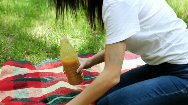 Young attractive dark-haired woman pouring fruit juice in a glass on a picnic in a park. HD